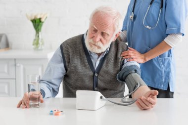 Nurse measuring blood pressure of calm grey haired man  clipart
