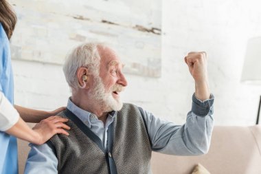 İşitme cihazı ile mutlu kıdemli adam uzağa bakıyor, evde oturuyor