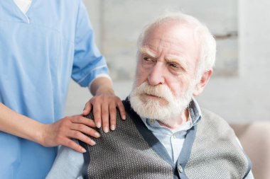 Nurse putting hands on shoulder of sad grey haired man clipart