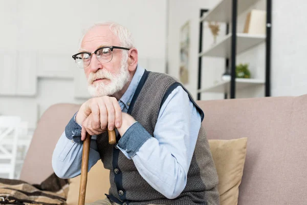 带着胡子和灰色头发的男人坐在明亮的房间里 把手放在拐杖上 — 图库照片