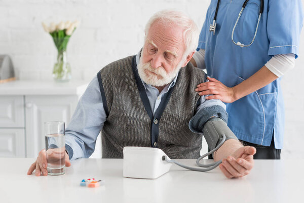 Nurse measuring blood pressure of calm grey haired man 