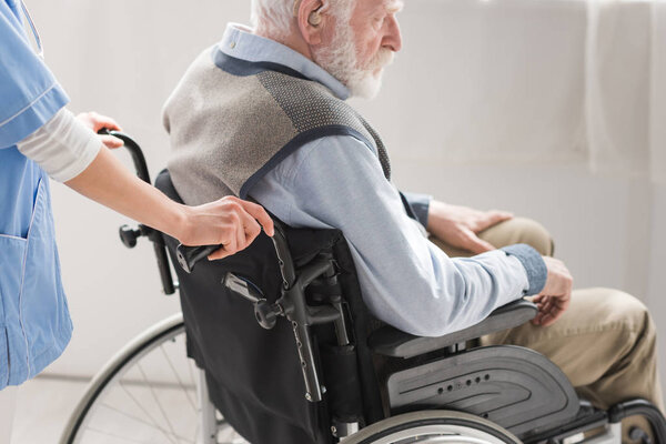Cropped view of nurse standing behind disabled senior man in wheelchair 