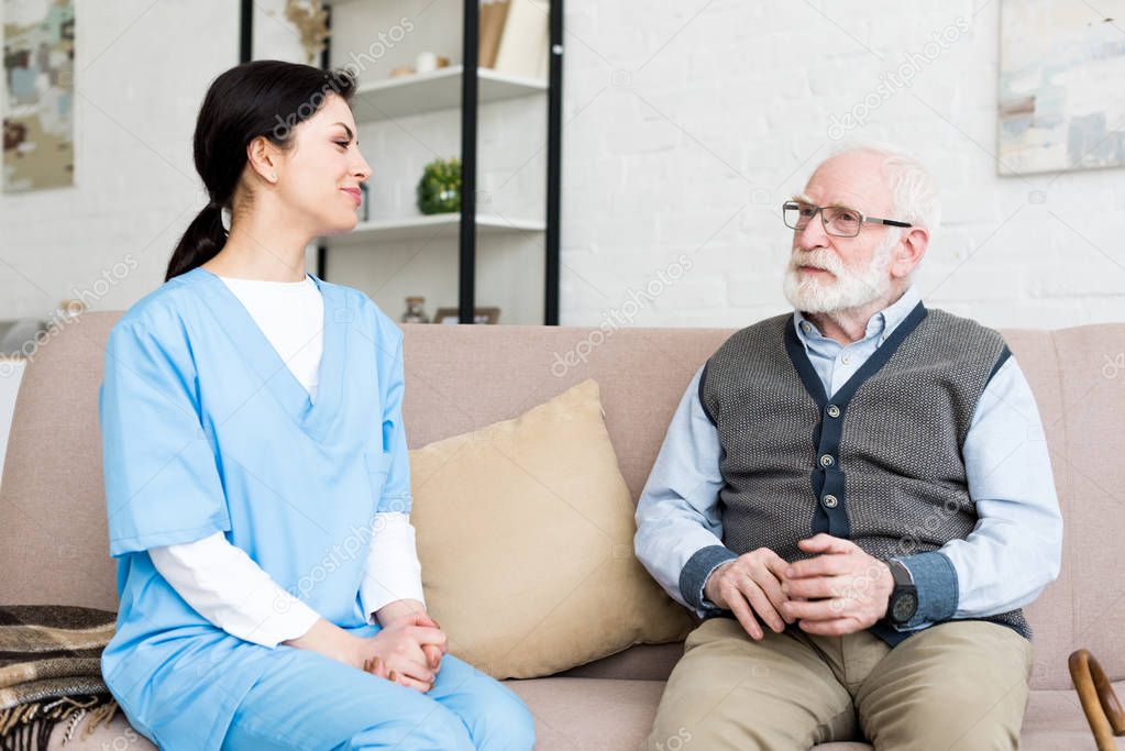 Happy nurse sitting on couch, looking at grey haired man