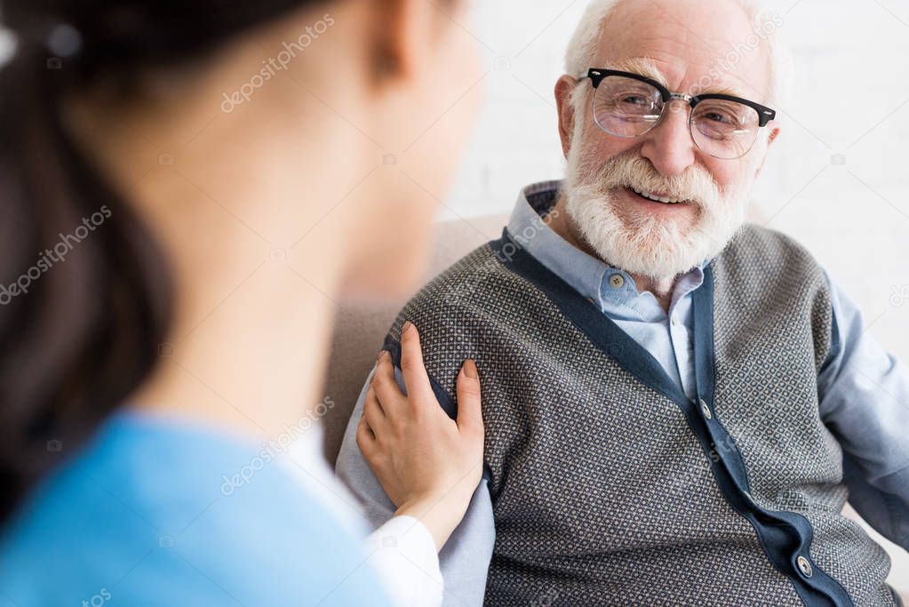 Selective focus of happy grey haired man looking at nurse
