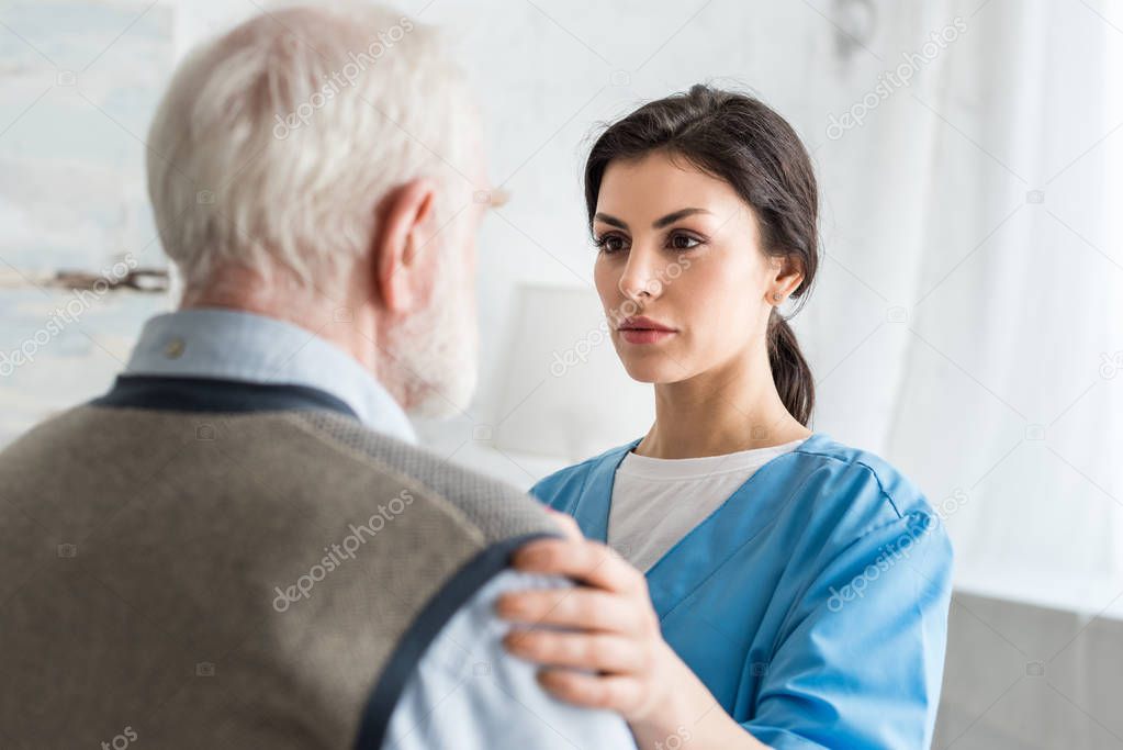 Selective focus of serious nurse putting hands on grey haired man