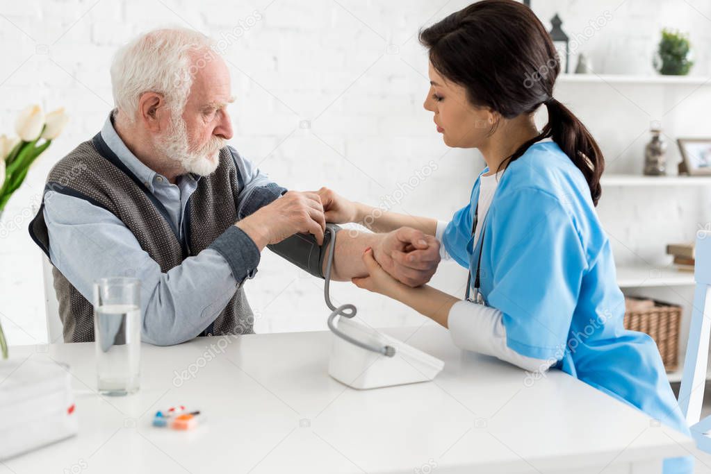 Adult nurse measuring blood pressure of grey haired man