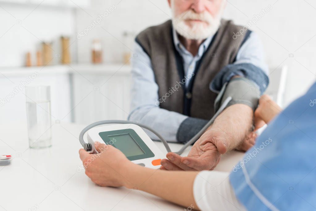 Cropped view of senior man and nurse measuring blood pressure