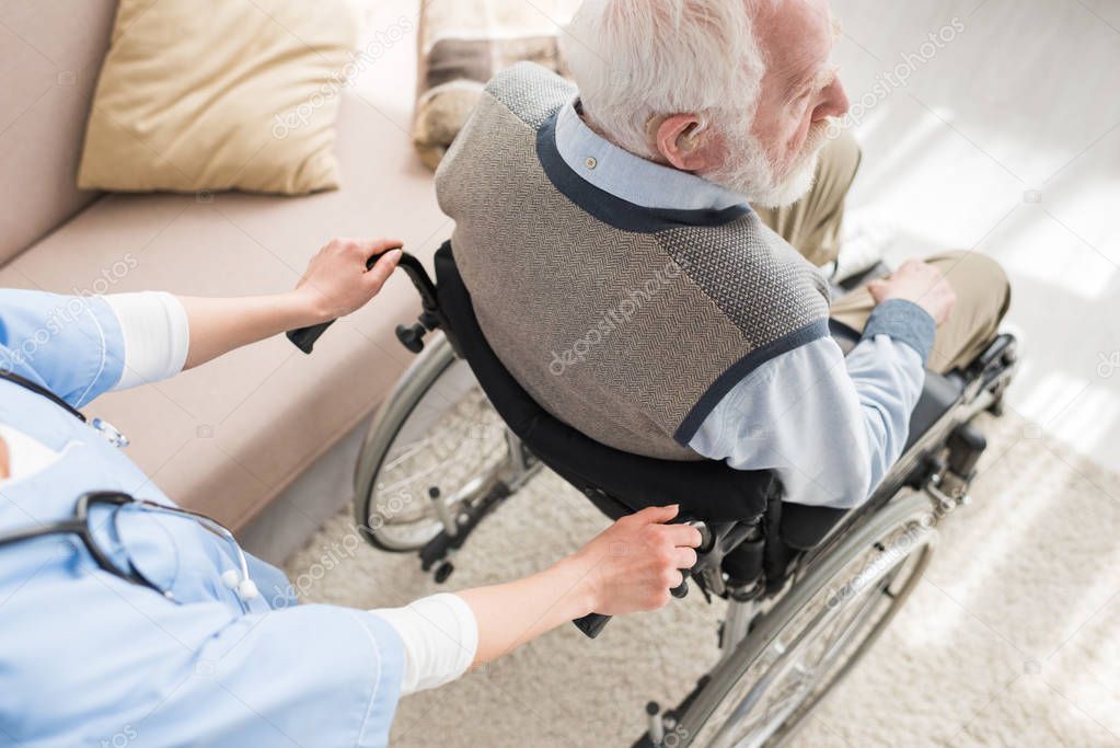 High angle view of nurse standing behind disabled gray haired man in wheelchair