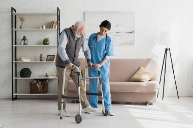 Nurse helping to senior man walking at home, recovering after injury clipart