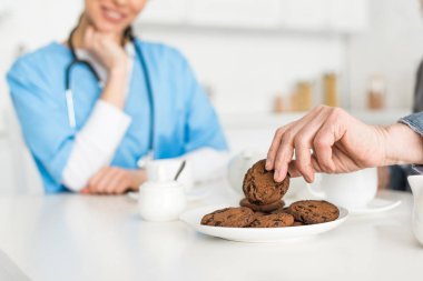 Selective focus of man hand with cookie and nurse on background clipart