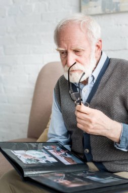 Sakin kıdemli adam elinde fotoğraf albümü ve gözlük tutarak