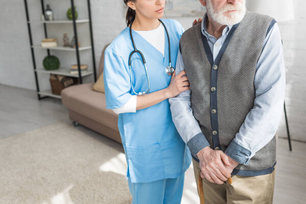 Cropped view of grey haired man standing with nurse in bright room