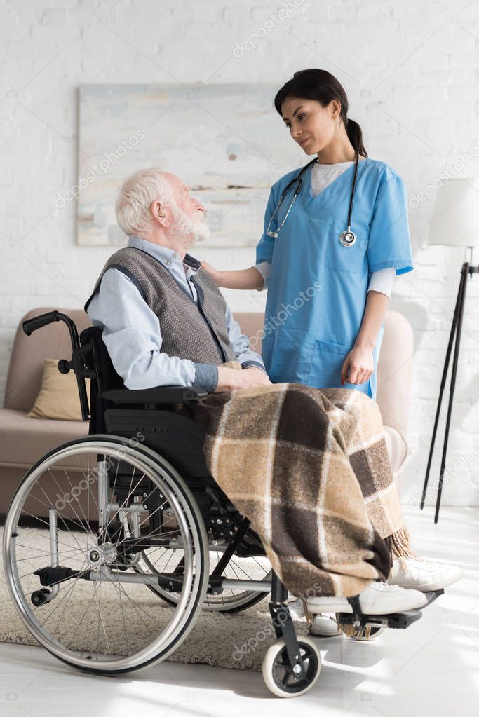 Nurse putting hands on disabled grey haired man in wheelchair