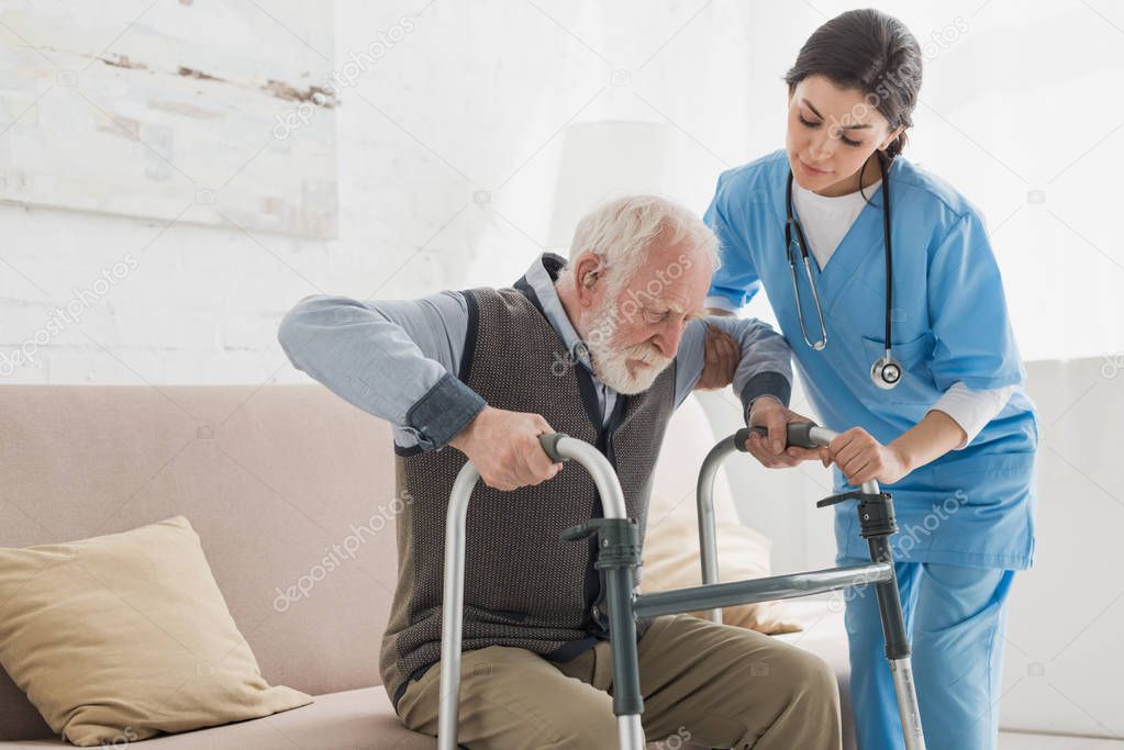Doctor helping to retired man, getting up from sofa