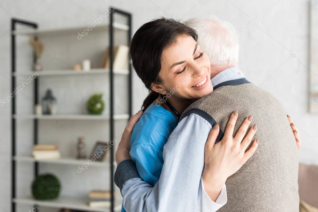 Smiling nurse hugging with grey haired man, standing in room