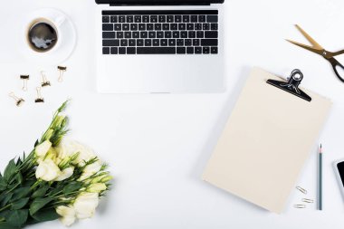 dizüstü bilgisayar, kahve fincanı, pano, çiçek, makas, kalem, bağlayıcı klipler ve beyaz ataş üst görünümü