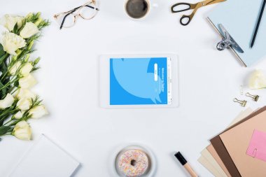 Kiev, Ukrayna - 11 Mayıs 2019: beyaz ekranda twitter uygulaması ile kahve, çörek, çiçek, gözlük, kitap, kağıtlar, pano ve dijital tablet fincan üst görünümü