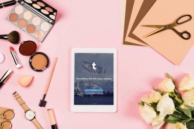 KYIV, UKRAINE - MAY 11, 2019: top view of digital tablet with tumblr app on screen, decorative cosmetics, flowers, craft paper and scissors on pink clipart