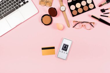Kiev, Ukrayna - 11 Mayıs 2019: pembe ekranda uber uygulaması ile dizüstü bilgisayar, dekoratif kozmetik, gözlük, kol saati, kredi kartı ve akıllı telefon üst görünümü
