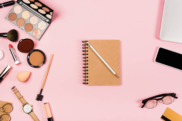 top view of notebook with pencil, glasses, smartphone with blank screen, credit card, accessories and decorative cosmetic on pink