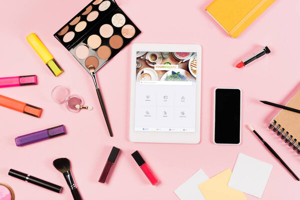 KYIV, UKRAINE - MAY 11, 2019: top view of digital tablet with foursquare app on screen, smartphone with blank screen, highlighters and decorative cosmetics on pink