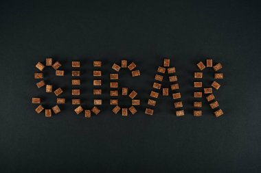 top view of word sugar made of unrefined brown sugar cubes on black background  clipart