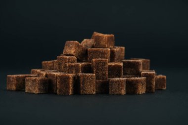pile of unrefined brown sugar cubes on black background clipart