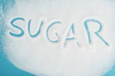 top view of word sugar made on sprinkled white sugar crystals on blue surface clipart