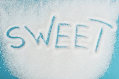 top view of word sweet made on sprinkled white sugar crystals on blue surface clipart