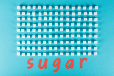 top view of red paper cut word sugar near rows of sugar cubes on blue surface clipart