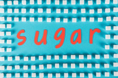 mavi yüzeyüzerinde beyaz şeker küpleri ile çevrili kırmızı kağıt kesme kelime şeker üst görünümü