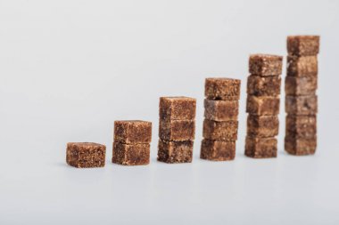 gri arka plan üzerinde yığınlar halinde düzenlenmiş kahverengi şeker küpleri 