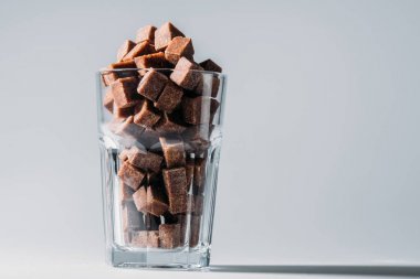 glass with unrefined brown sugar cubes on grey background clipart