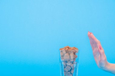 cropped view of woman showing refuse gesture near glass with brown sugar cubes isolated on blue clipart