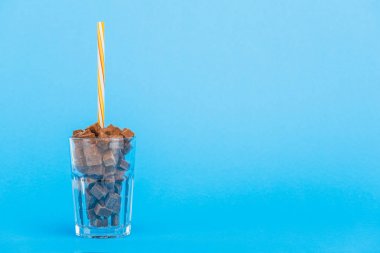 brown sugar cubes in glass with straw on blue background with copy space clipart