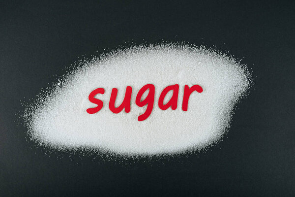top view of paper cut word sugar on white sugar crystals on black background