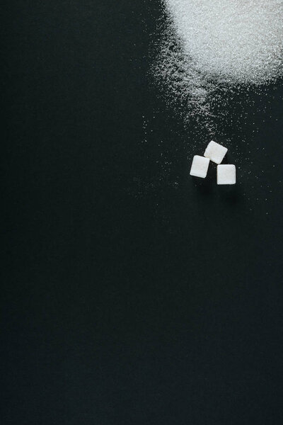 top view of white sugar crystals and cubes on black background with copy space