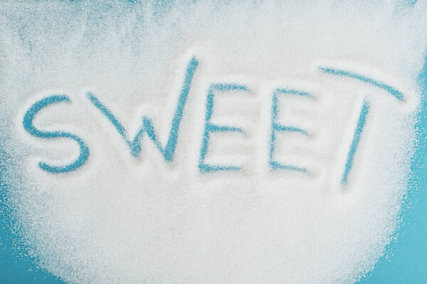 top view of word sweet made on sprinkled white sugar crystals on blue surface