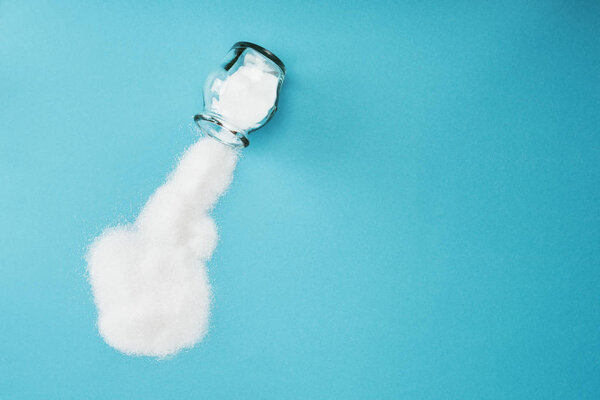 top view of glass jar with sprinkled white sugar crystals on blue background with copy space