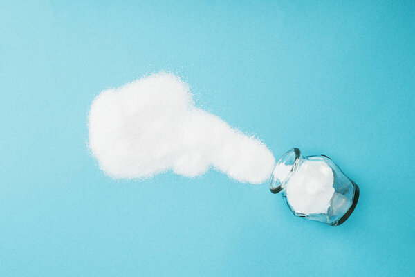 top view of white sugar crystals near glass jar on blue background 