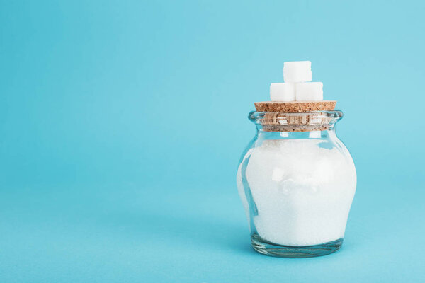 white sugar cubes on corked glass jar with sugar on blue background
