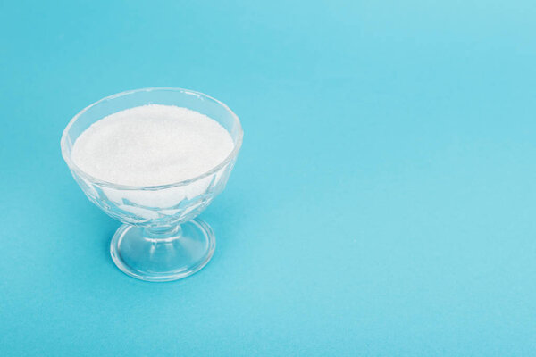 glass bowl with white granulated sugar on blue background with copy space