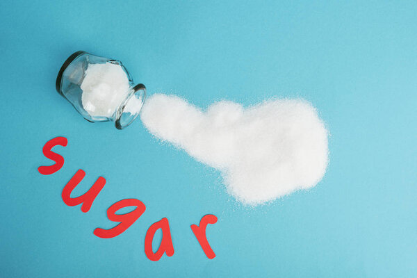 top view of red paper cut word sugar near glass jar and sprinkled sugar crystals on blue background
