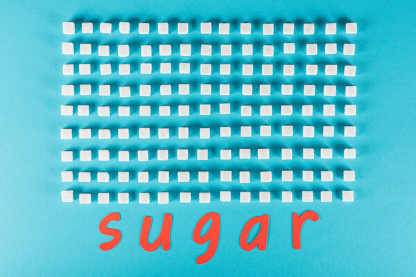 top view of red paper cut word sugar near rows of sugar cubes on blue surface