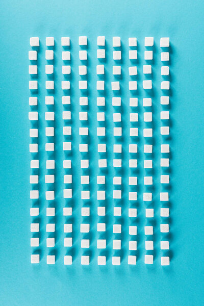 top view of white sugar cubes arranged in rows on blue surface