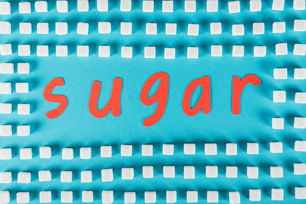 top view of red paper cut word sugar surrounded by white sugar cubes on blue surface