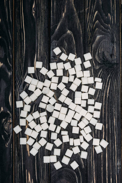 top view of white sugar cubes on black wooden background 