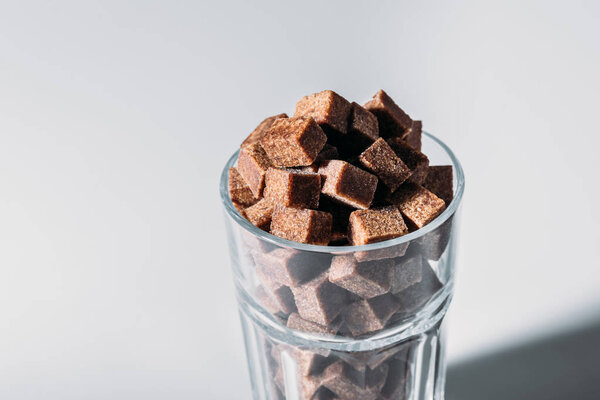 стакан, полный коричневых кубиков сахара на сером фоне
