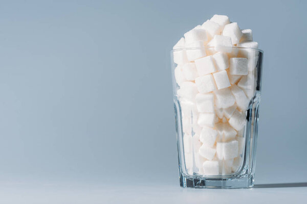 glass full of refined white sugar cubes on grey background with copy space