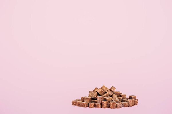 куча коричневых кубиков сахара на розовом фоне с копировальным пространством
